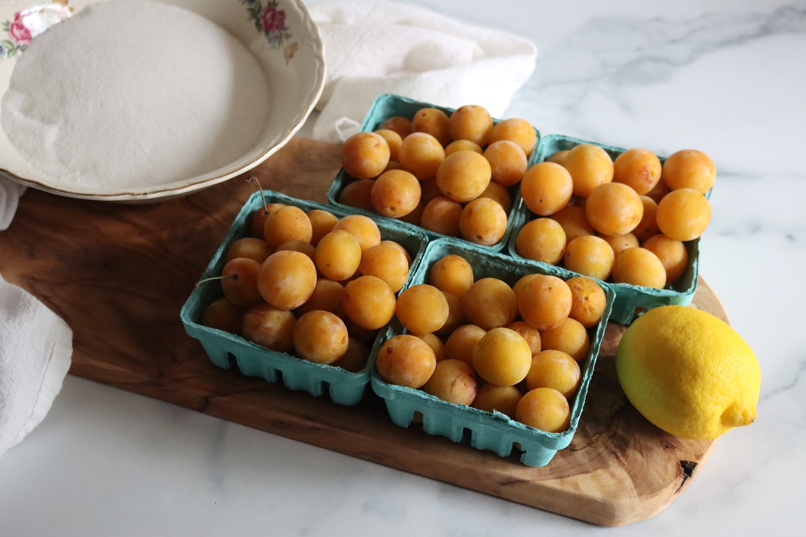Fresh mirabelle plums in berry baskets with a bowl of sugar and a lemon