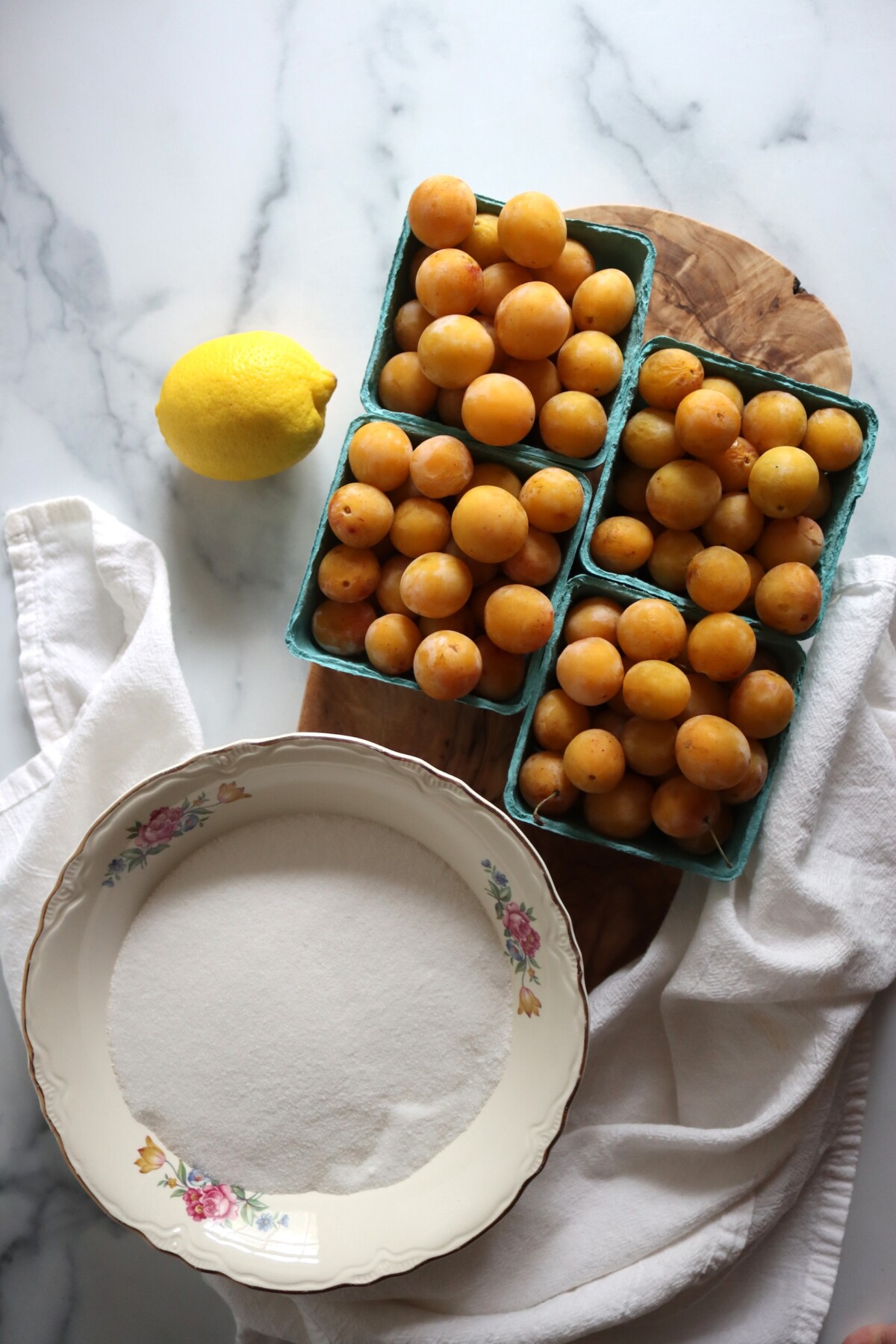Mirabelle plums in green berry baskets with sugar and a lemon on a marble counter