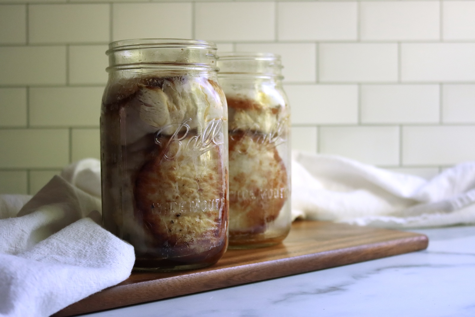 Browned pork chops packed into a quart jar and a pint jar for pressure canning