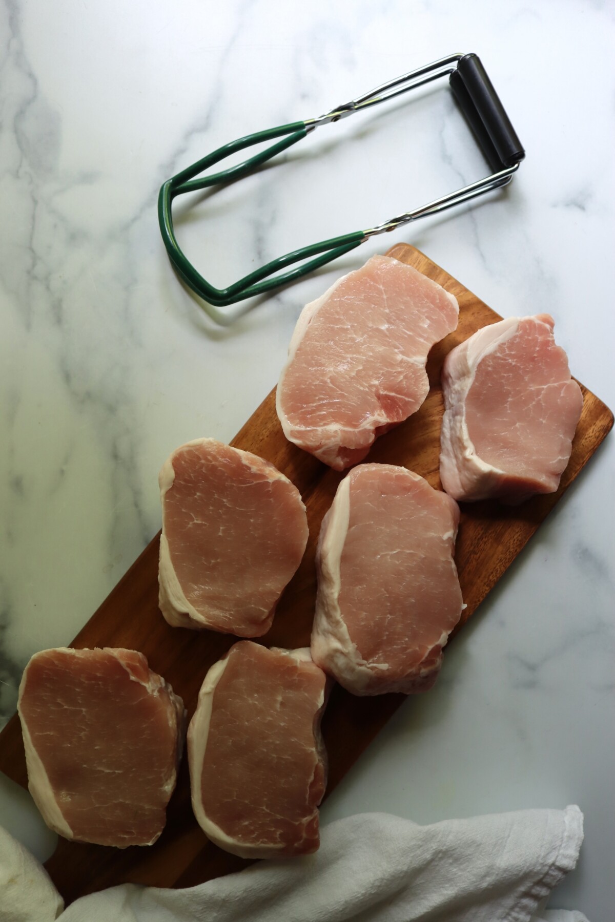 Raw boneless pork chops on a wooden cutting board, ready to trim and slice for canning
