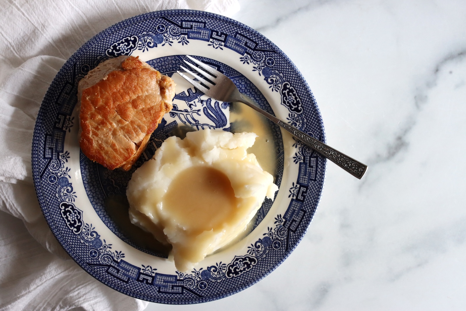 Browned canned pork chop with mashed potatoes and gravy on a blue and white plate