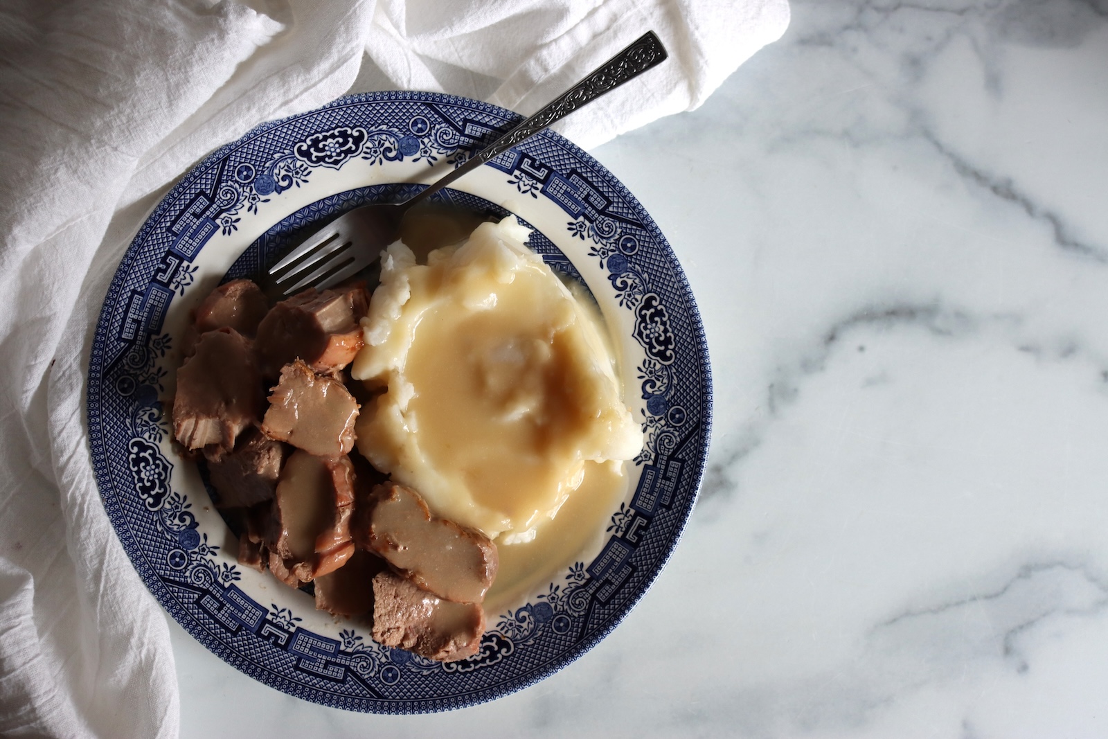 Plate of canned pork tenderloin with gravy and mashed potatoes on a marble counter