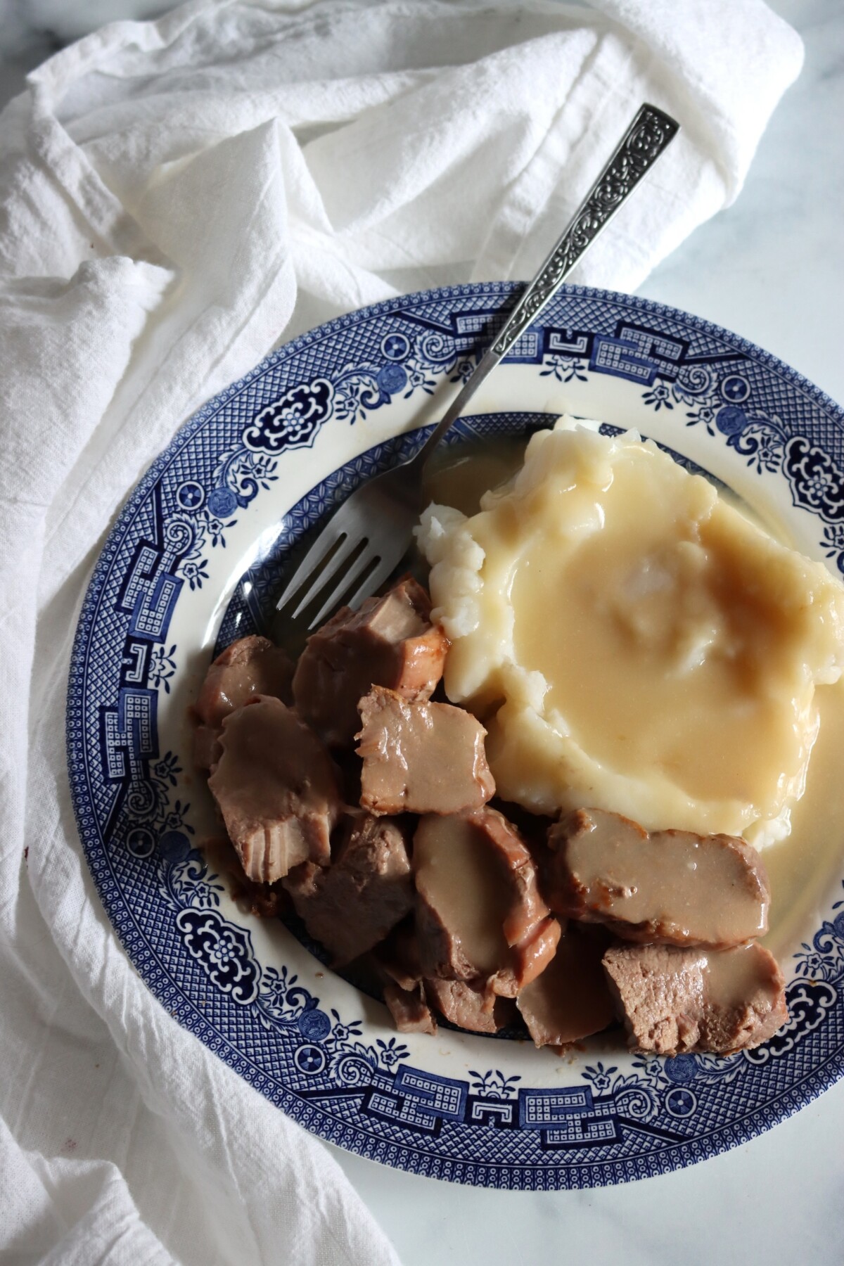 Canned pork tenderloin medallions in gravy with mashed potatoes on a blue and white plate