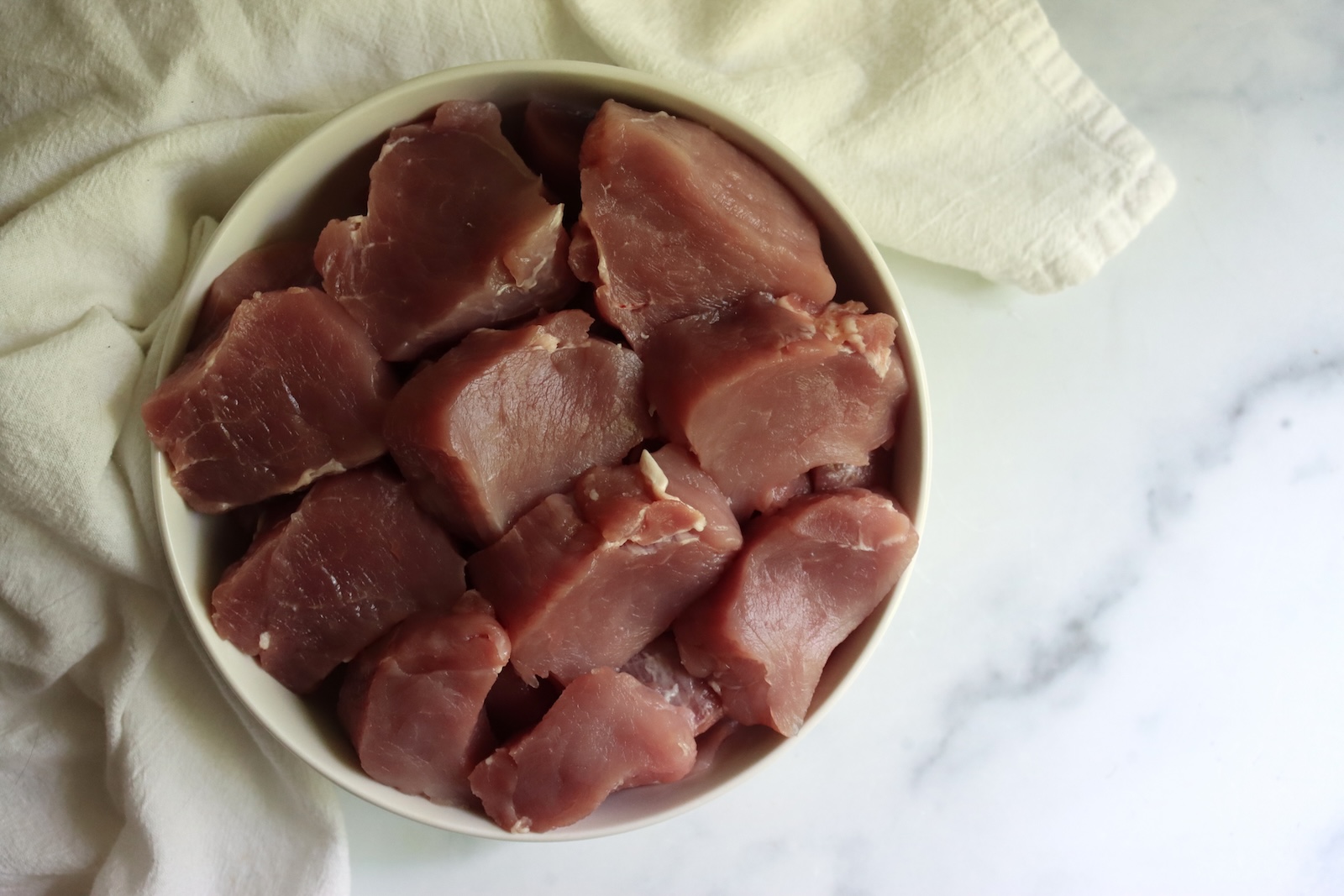 Raw pork tenderloin cut into chunks in a white bowl for a raw pack