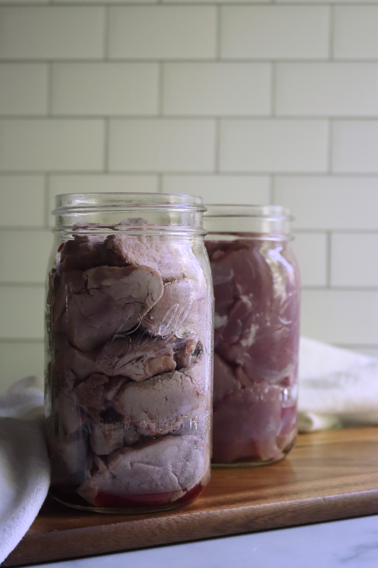 Quart jars packed with pork tenderloin before canning, hot pack medallions in front and raw pack behind