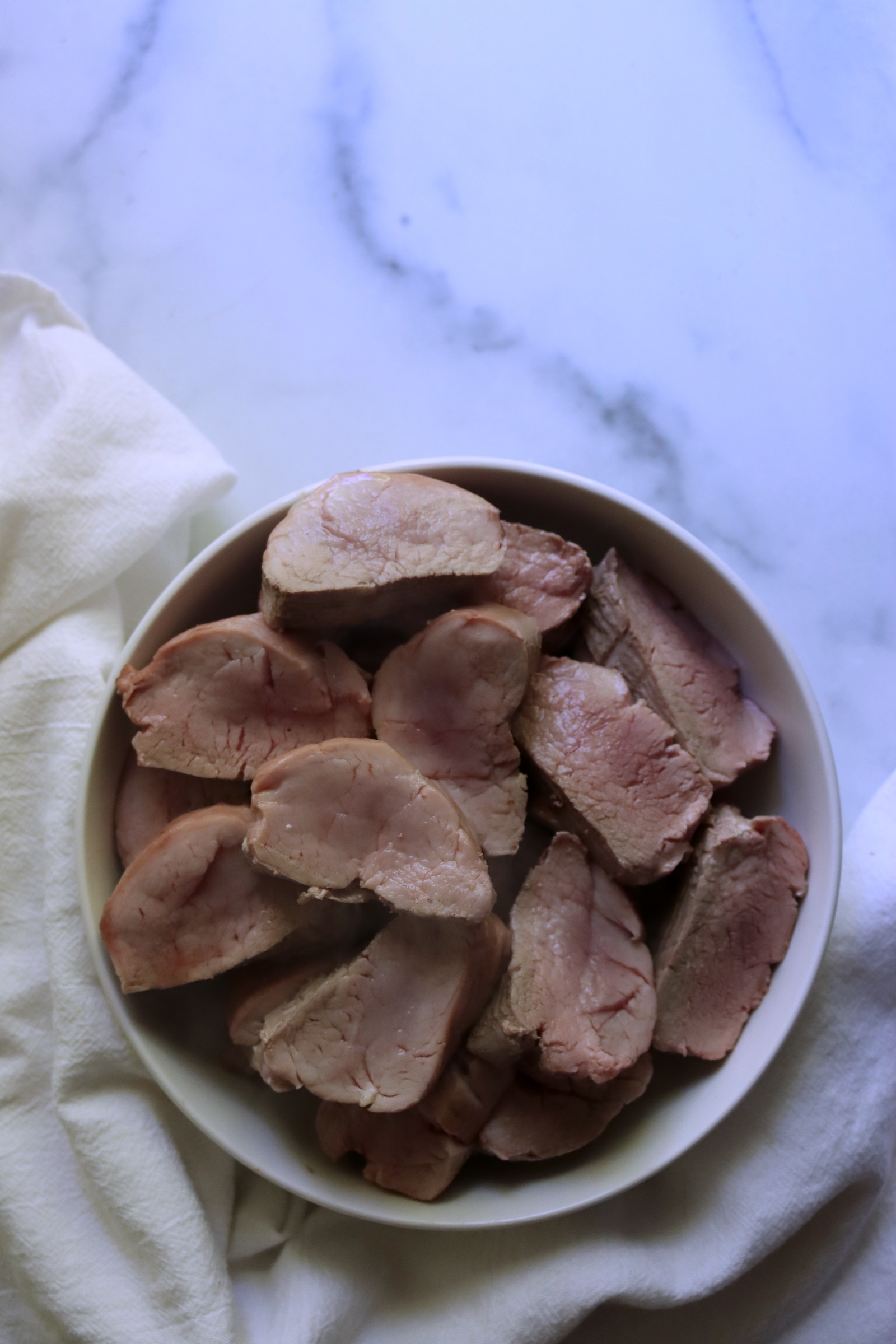 Roasted pork tenderloin sliced into medallions in a white bowl, still pink in the center